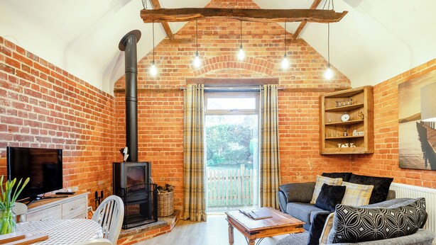 A cozy living room with a brick fireplace, a television, and comfortable seating. - 1 bedroom accommodation in Foulsham, near Reepham (Foulsham, near Reepham)