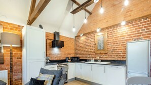 A kitchen with white cabinets, a stove, and a refrigerator. There is a brick wall and a wooden ceiling. - 1 bedroom accommodation in Foulsham, near Reepham (Foulsham, near Reepham)