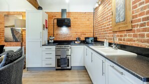 A kitchen with white cabinets, a stove, a microwave, and a brick wall. - 1 bedroom accommodation in Foulsham, near Reepham (Foulsham, near Reepham)