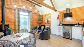 A cozy kitchen and dining area with exposed brick walls, wooden beams, and a modern stove. - 1 bedroom accommodation in Foulsham, near Reepham (Foulsham, near Reepham)
