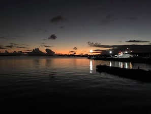 Waterfront views of a tranquil body of water reflecting the sky, with a dock and a building in the background.