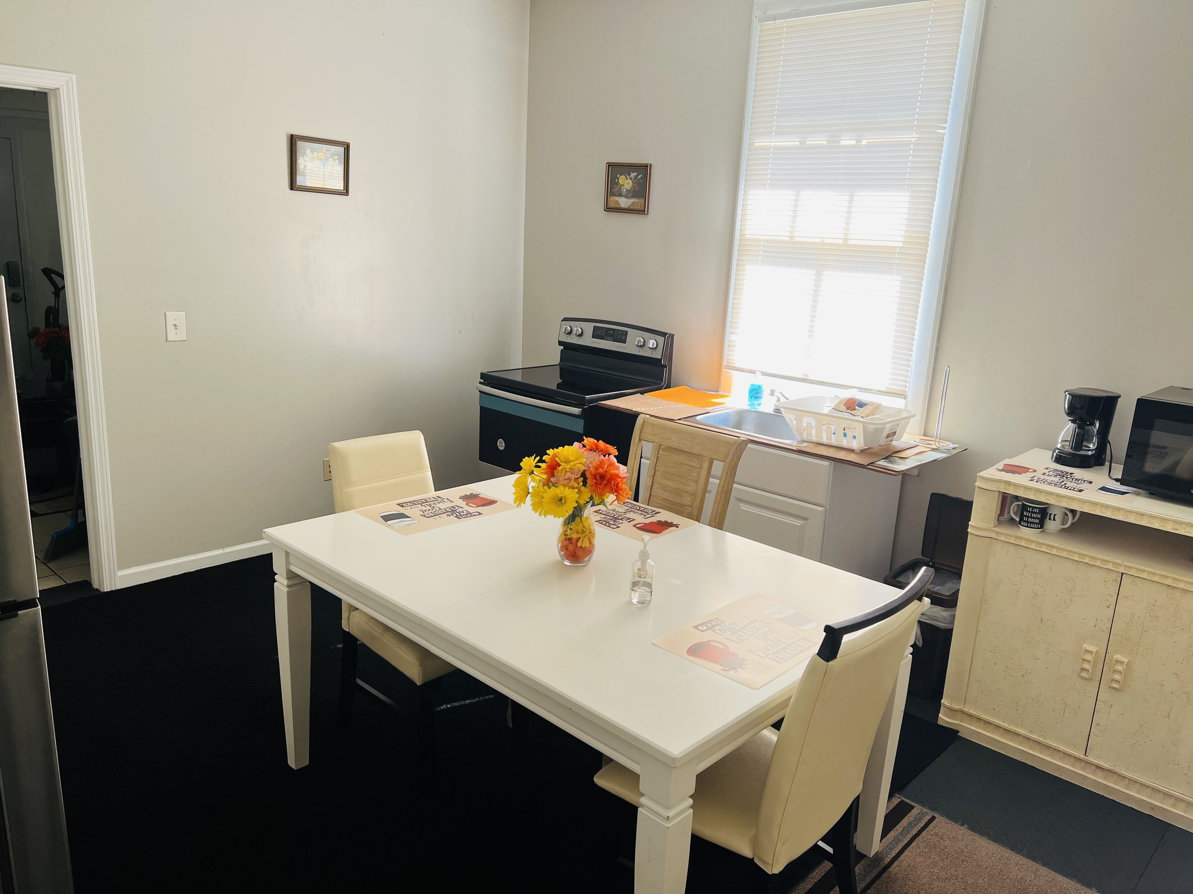 A compact kitchen with a dining table, chairs, a refrigerator, a stove, and a window with blinds.