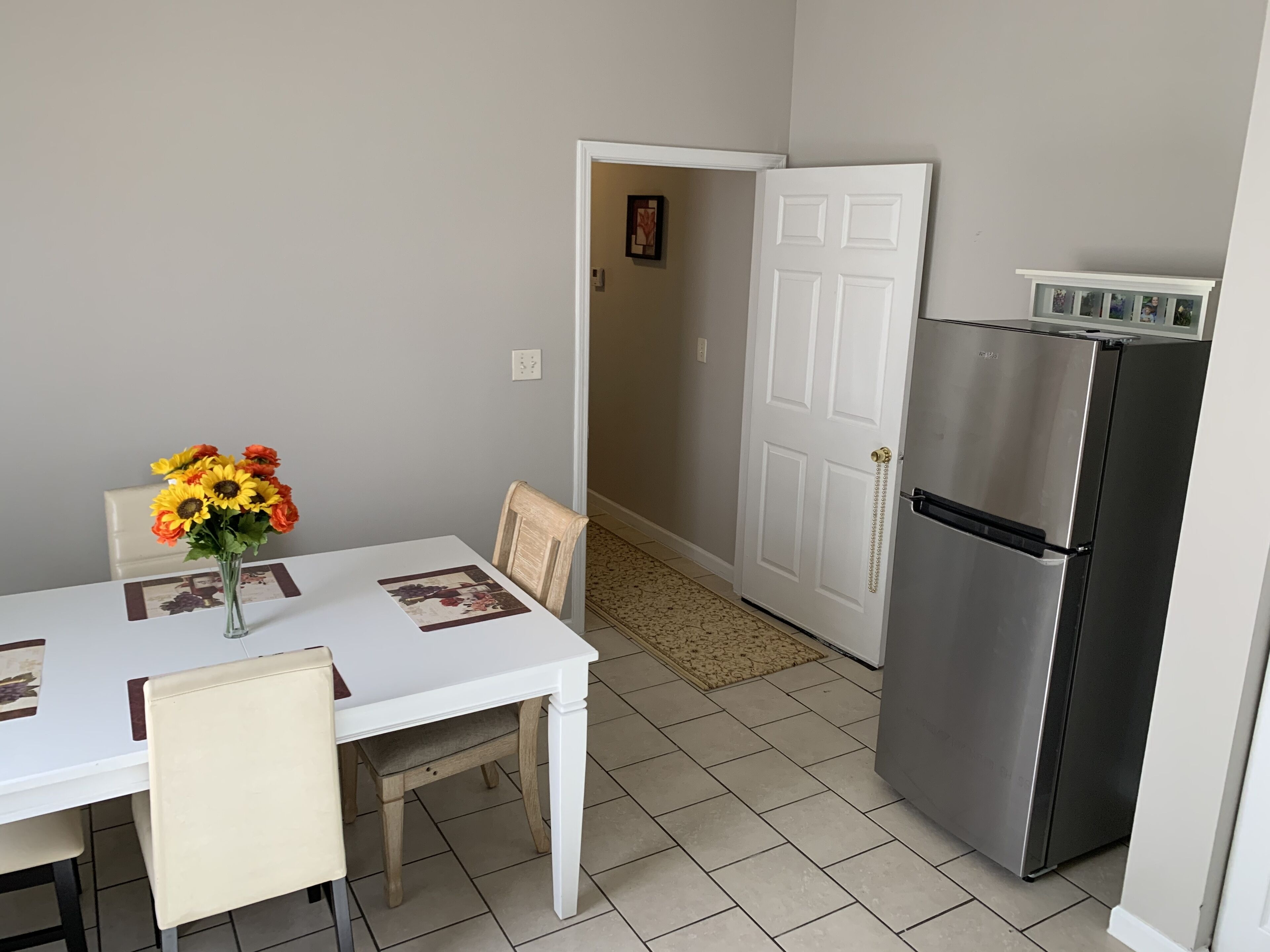 Eine kleine Küche mit einem weißen Kühlschrank, einem Esstisch mit Stühlen und einer Blumenvase.