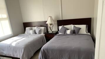 Un dormitorio con dos camas, una mesita de noche con lámpara y una ventana con persianas.