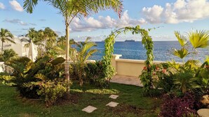 A garden with a pathway leading to a view of the sea, palm trees, and a ship in the distance. - The CLIFF - 4th-floor Luxury Condo on the Beach - Luxury Beachfront Resort  (Cupecoy)