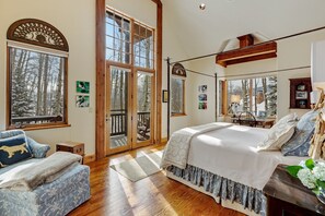 Relax in a serene bedroom with a large bed, wooden bench, and chest of drawers, offering a peaceful view of the surrounding trees.
