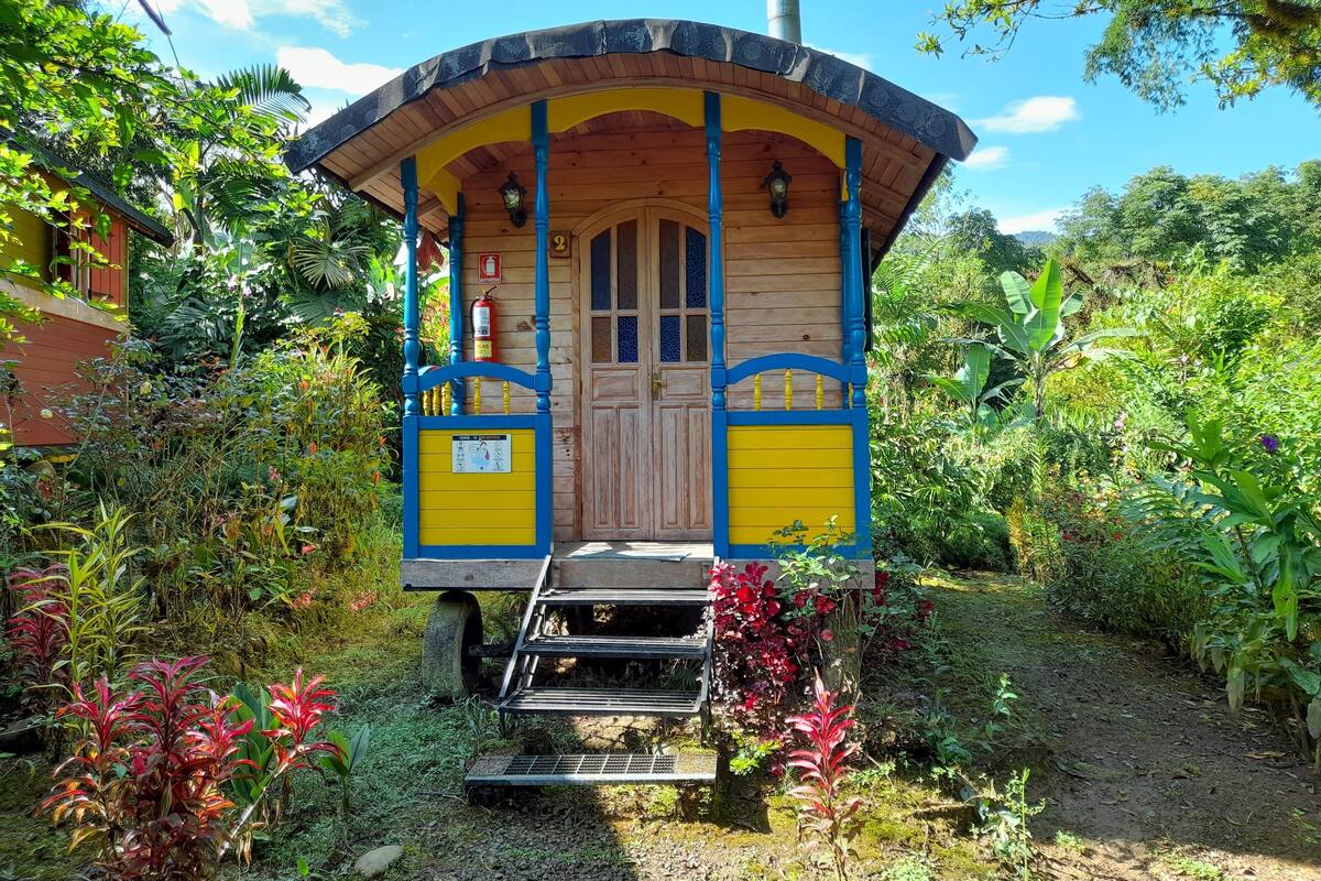 A small, wooden structure with a yellow and blue facade, a door, and a ramp leading to the entrance.