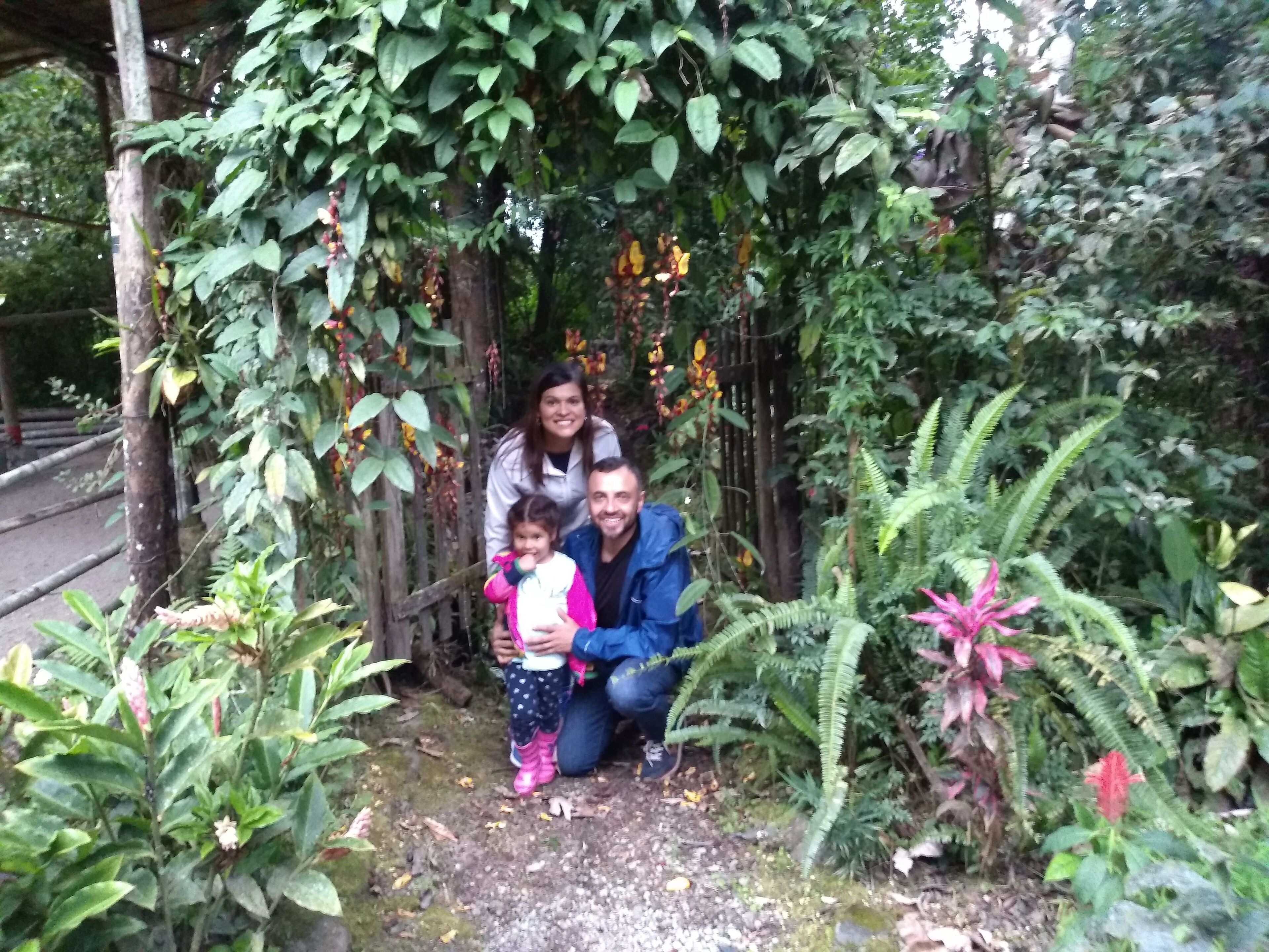 A family of four in a garden with dense foliage and a wooden structure.