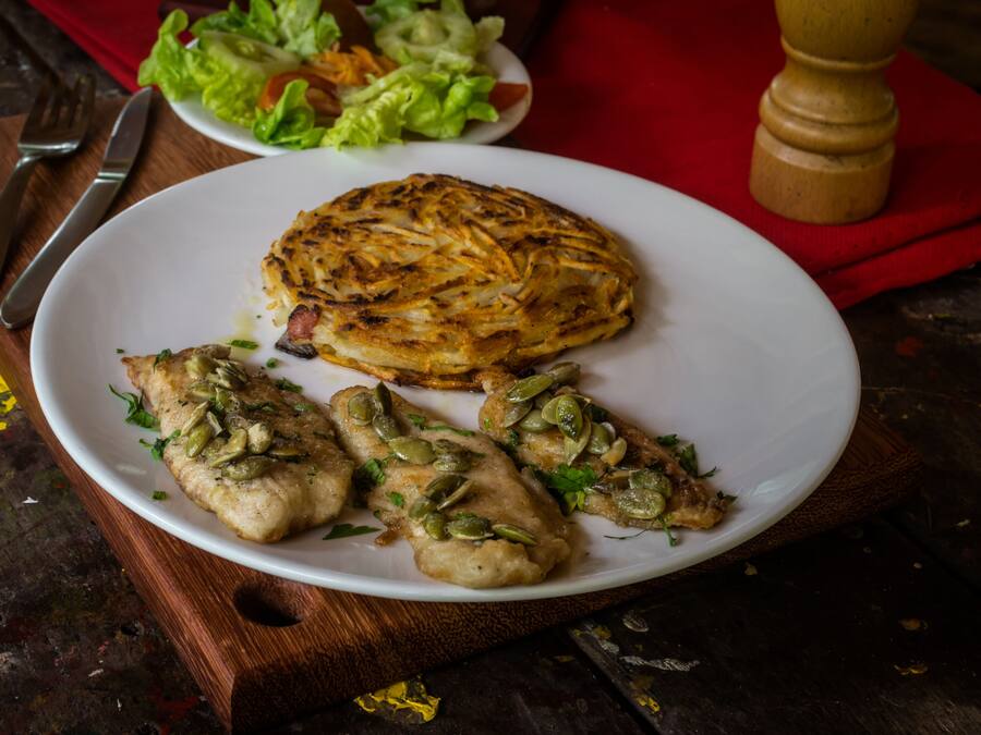 A plate with food, a fork, and a knife on a wooden table.