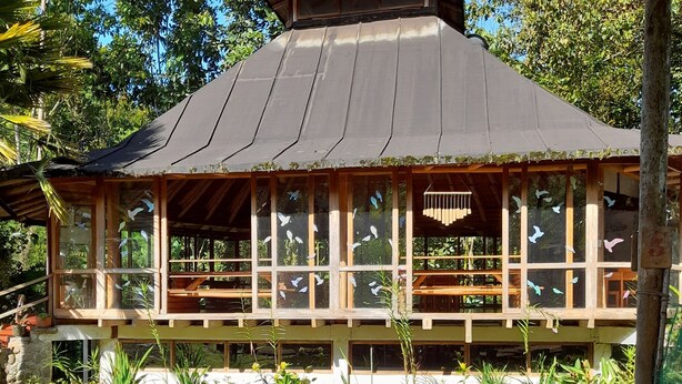 A traditional wooden structure with a sloped roof, surrounded by lush greenery and a well-maintained lawn. - Hosteria La Roulotte Mindo (Mindo)