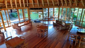 A spacious wooden interior with multiple seating areas, large windows offering views of the surrounding greenery. - Hosteria La Roulotte Mindo (Mindo)