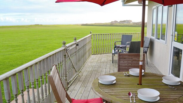 A wooden deck with a table and chairs, overlooking a green field. - 2 bedroom accommodation in Bacton (Bacton)