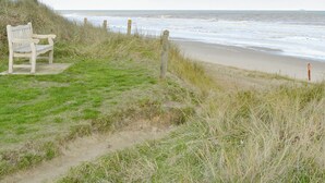 A bench on a grassy path beside a beach with waves. - 2 bedroom accommodation in Bacton (Bacton)