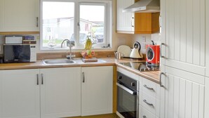 A kitchen with white cabinets, a microwave, a sink, a stove, and a window with a view of the outside. - 2 bedroom accommodation in Bacton (Bacton)