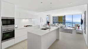Une cuisine moderne avec des meubles blancs, un îlot central et une vue sur l’océan grâce à de grandes fenêtres.
