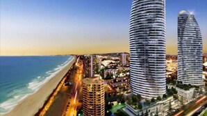 Un paysage urbain côtier avec deux imposants immeubles cylindriques, une plage et une zone urbaine densément peuplée où l’on peut voir des lampadaires.