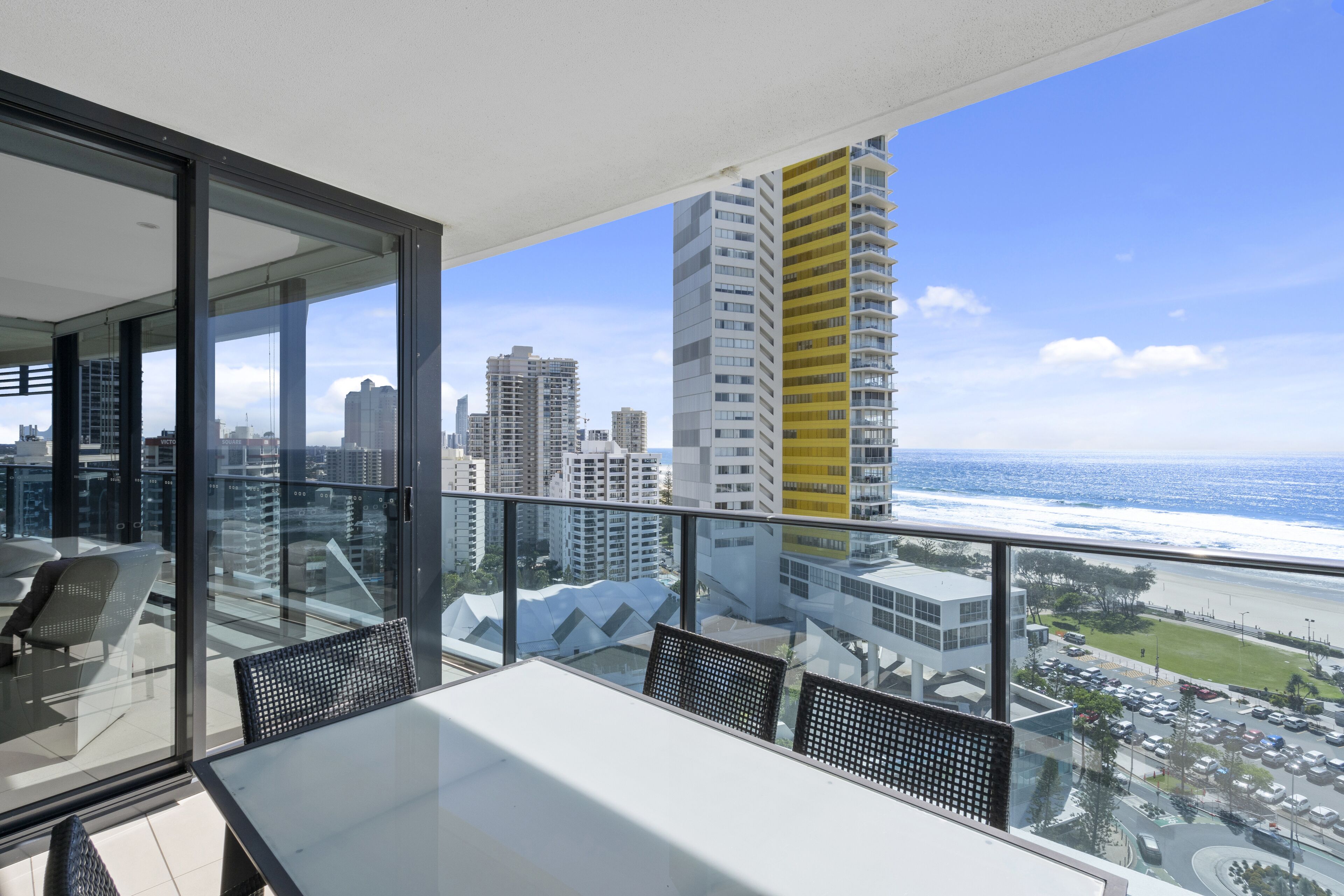 Uma varanda com guarda-corpo de vidro, vista para a paisagem urbana e o oceano.