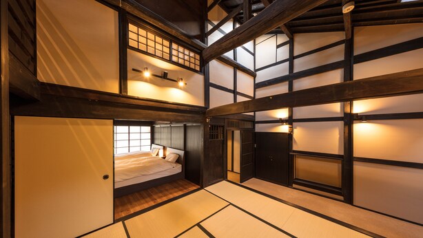 A traditional Japanese-style room with tatami flooring, a bed with white bedding, and wooden beams on the ceiling.
