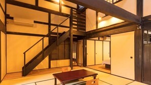 A traditional Japanese-style room with tatami flooring, a low wooden table, and a staircase with dark wooden beams.
