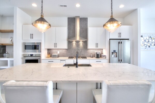 A modern kitchen with a large island, stainless steel appliances, and pendant lighting.