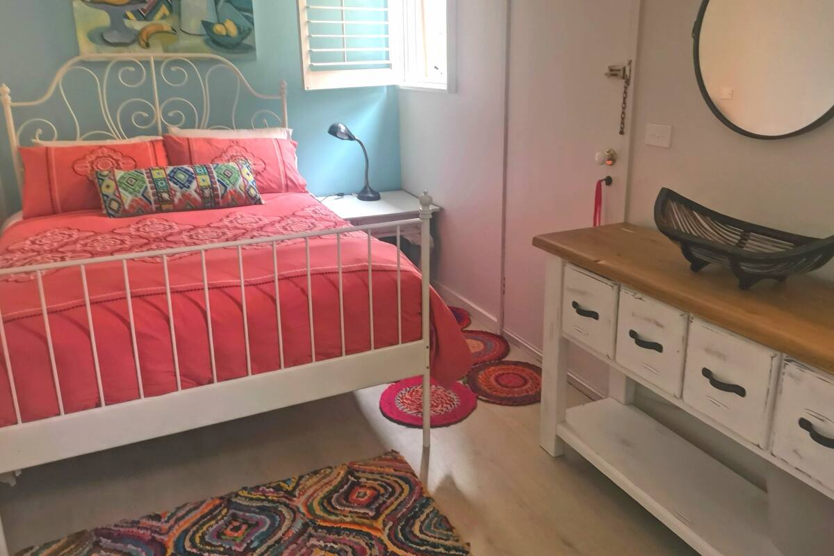 Um quarto com cama, mesa de cabeceira, abajur e cômoda.