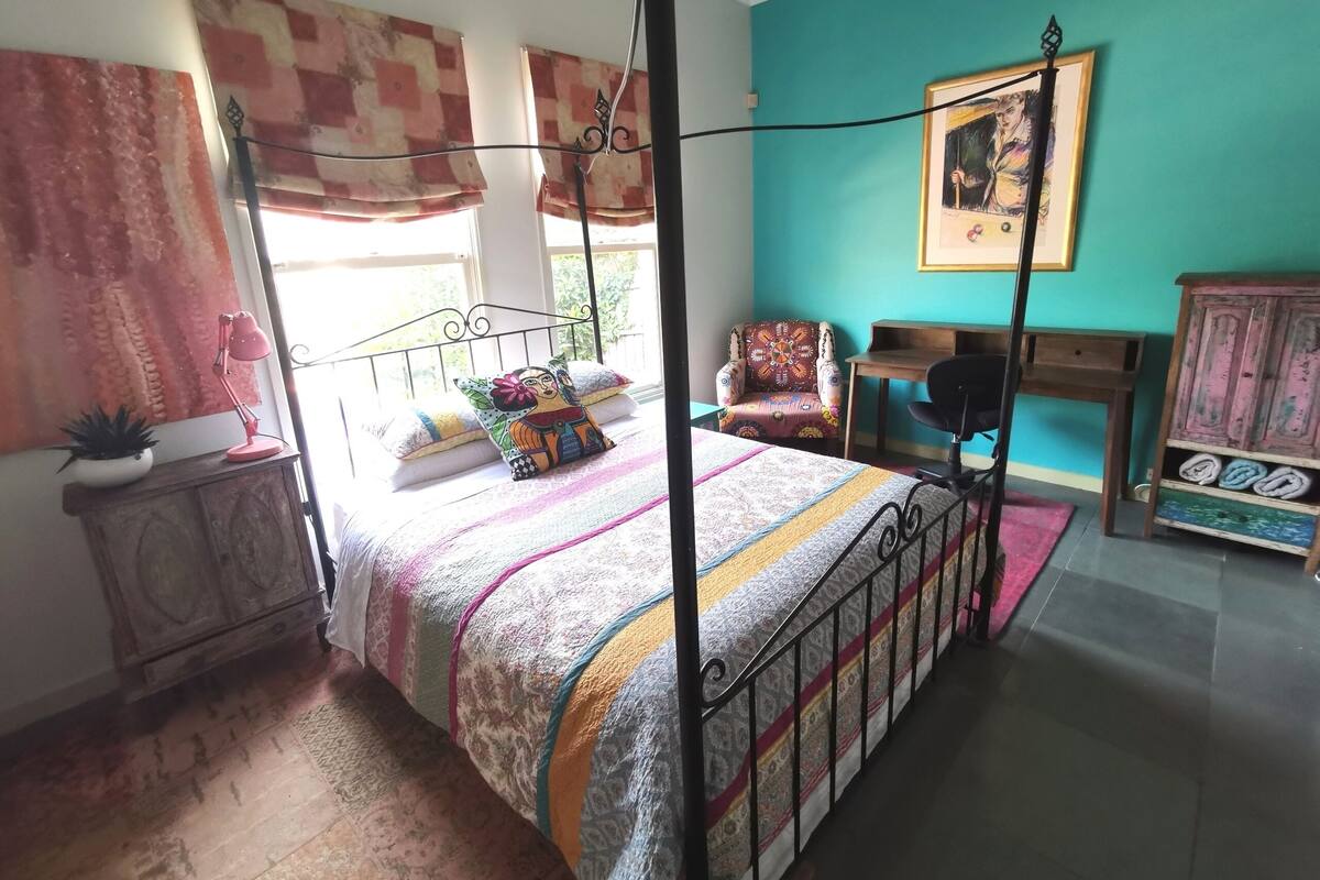 Quarto com cama de dossel, uma cadeira, escrivaninha e um armário.