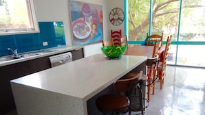 A kitchen with a white countertop, a green bowl, and wooden chairs. - Stylish Comfortable Central Artists Home (Glen Waverley)