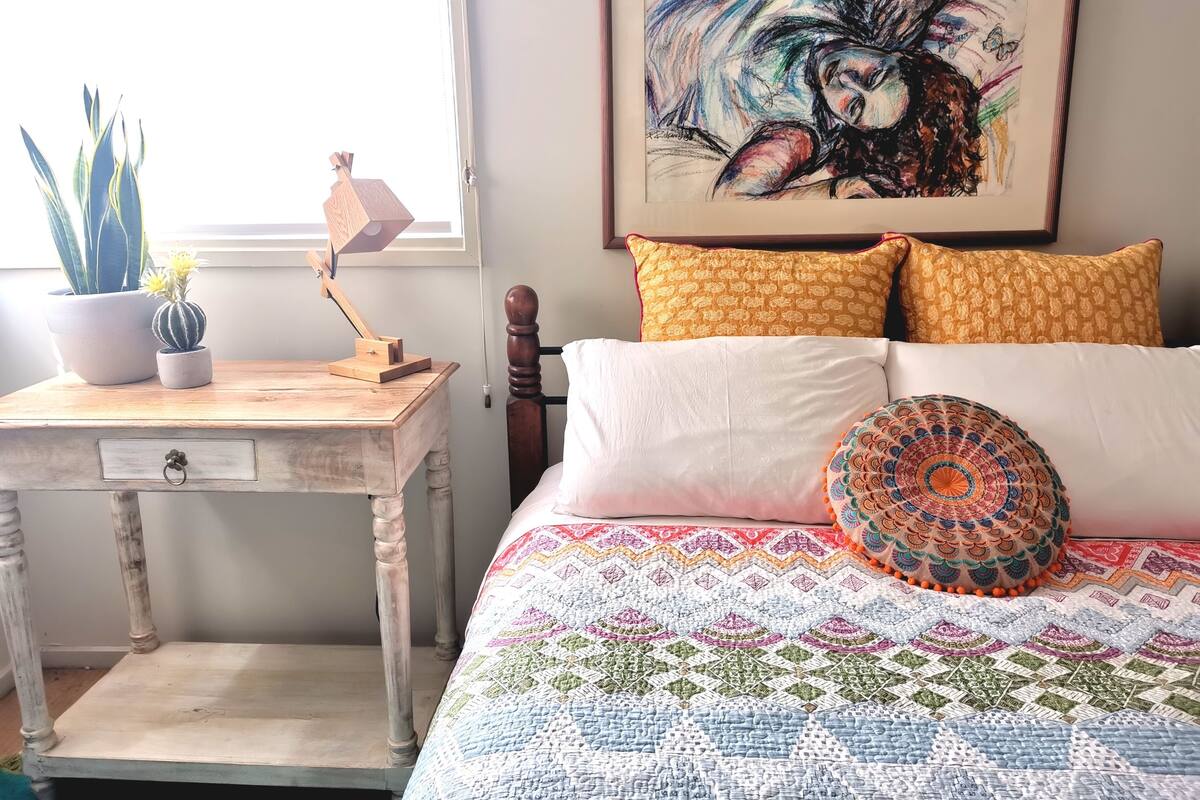 Um quarto com uma cama, uma escrivaninha, uma planta em vaso e um quadro na parede.