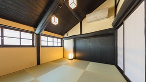 Une pièce avec un sol recouvert de tatamis, un plafond en bois, une porte coulissante et une petite table avec une lampe.