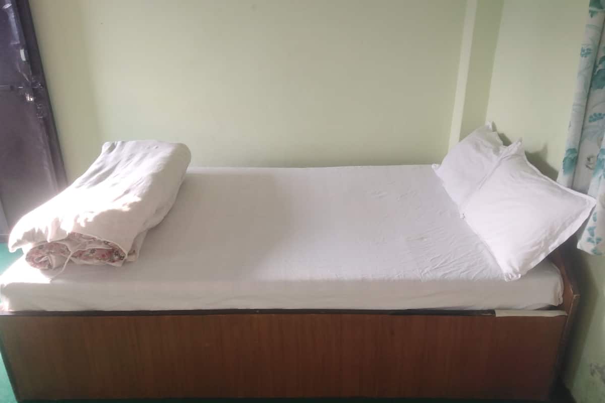 A single bed with white bedding and pillows, a wooden headboard, and a green floor.