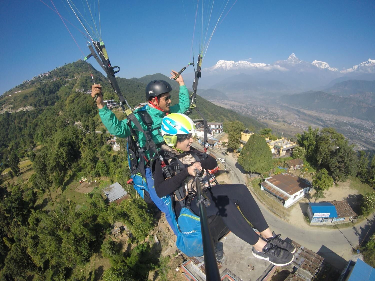 A person paragliding over a mountainous area with houses and greenery below.