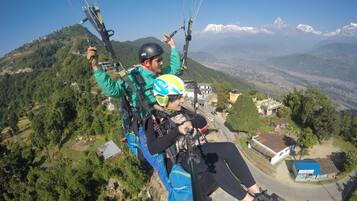 A person paragliding over a mountainous area with houses and greenery below.