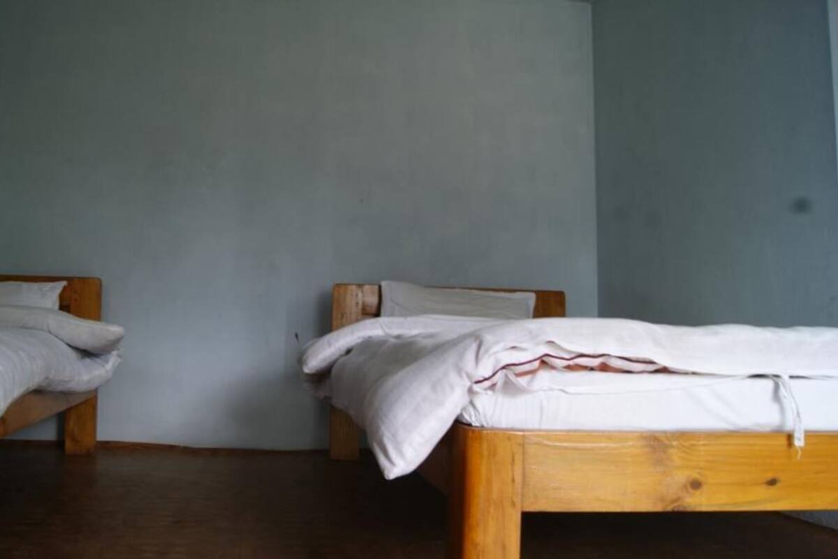 Two wooden beds with white bedding in a room with plain walls and a wooden floor.