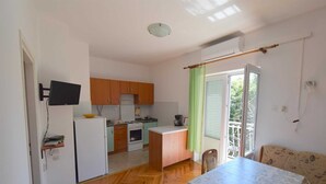 A compact kitchen with a refrigerator, stove, and sink, a dining area with a table and chairs, and a sliding glass door to a balcony. - Apartment Jelka 3 on the first floor (Njivice)
