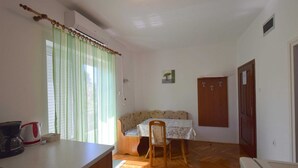 A small, well-lit room with a wooden floor, a table with a kettle, a chair, a sofa, and a door. - Apartment Jelka 3 on the first floor (Njivice)