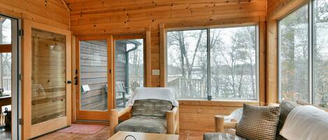 A wooden cabin interior with a cozy seating area, large windows, and a wooden ceiling.