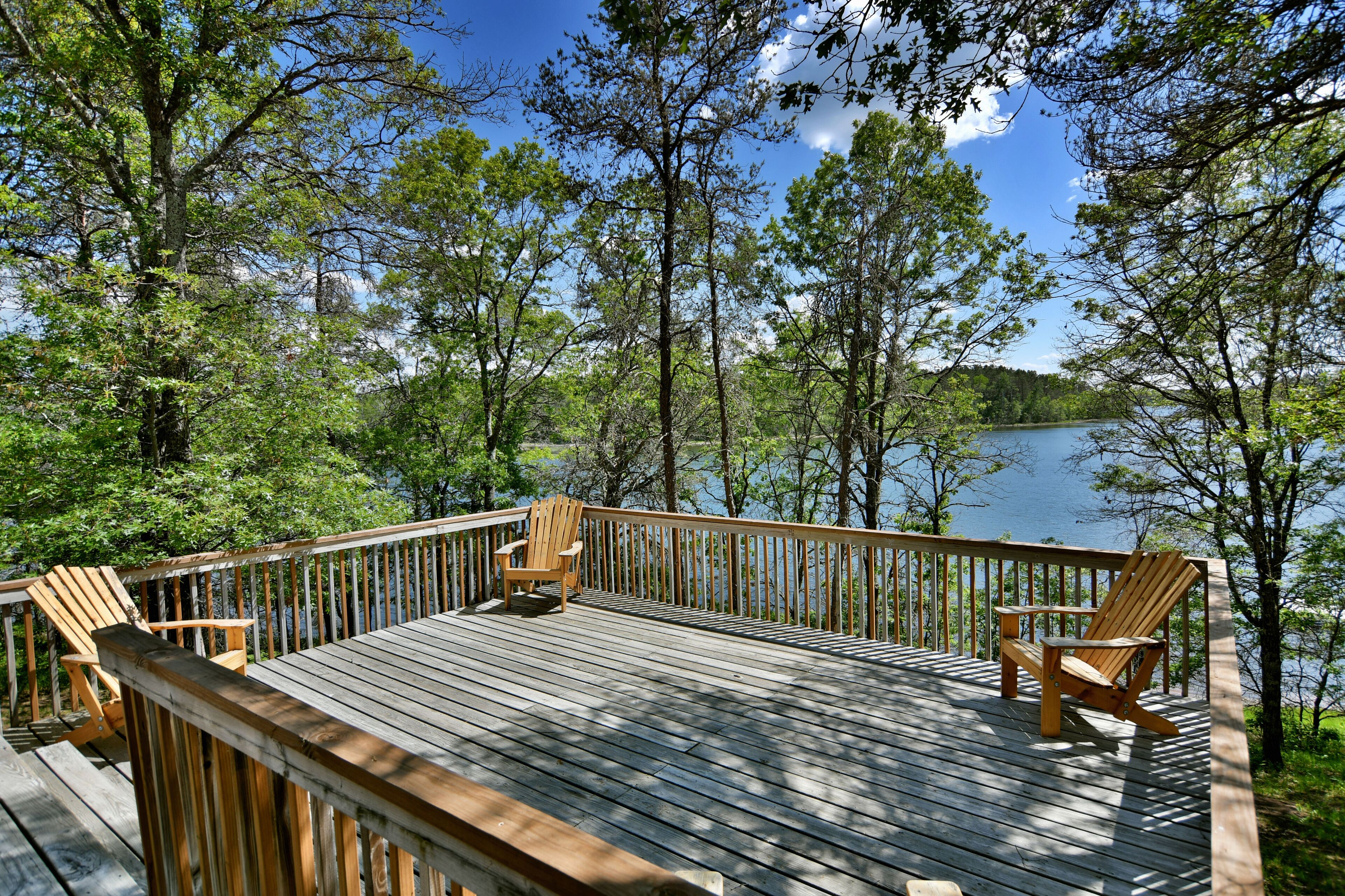 A wooden deck with two Adirondack chairs overlooking a lake surrounded by trees.