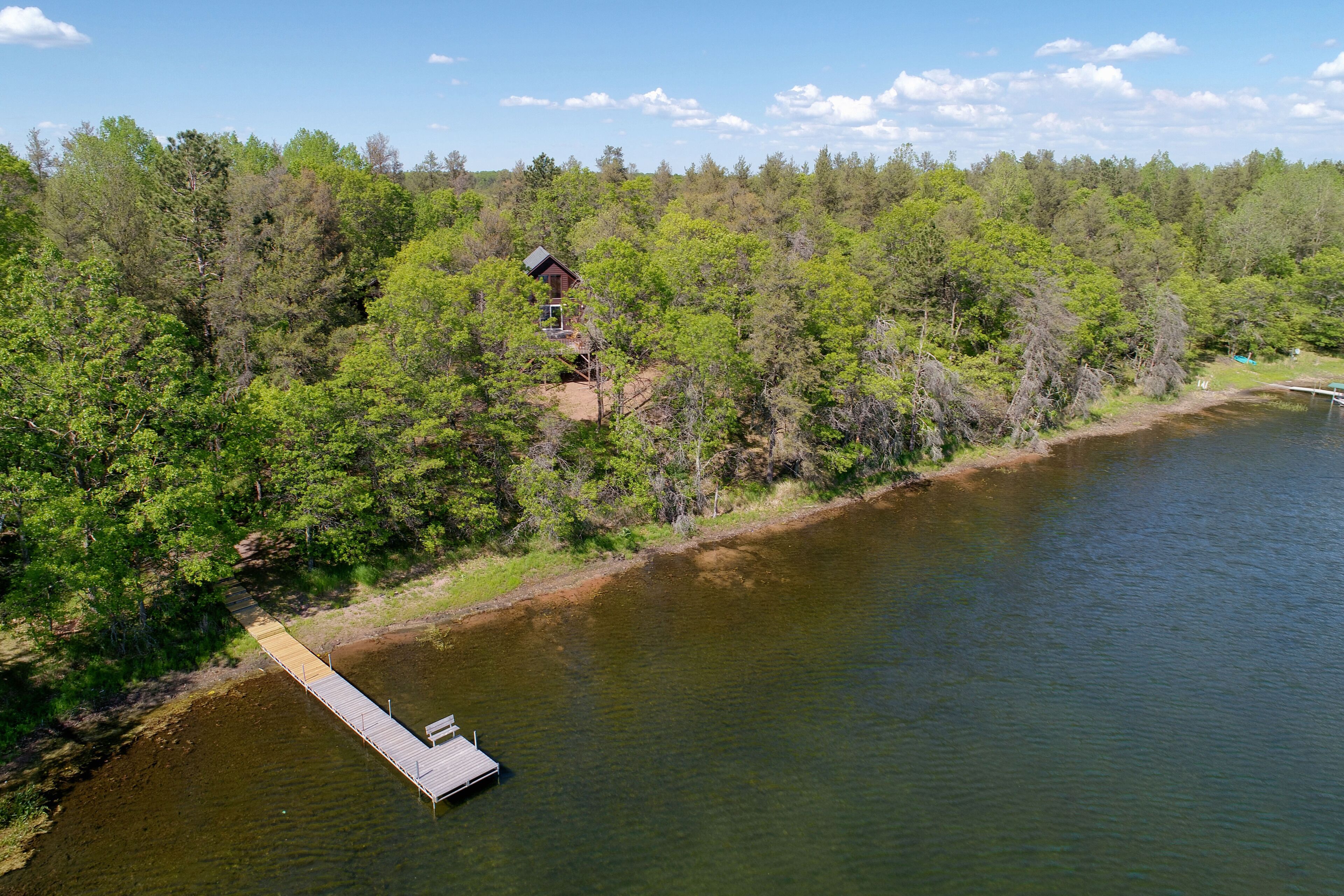 A lakeside cabin with a dock extending into the water, surrounded by dense forest.