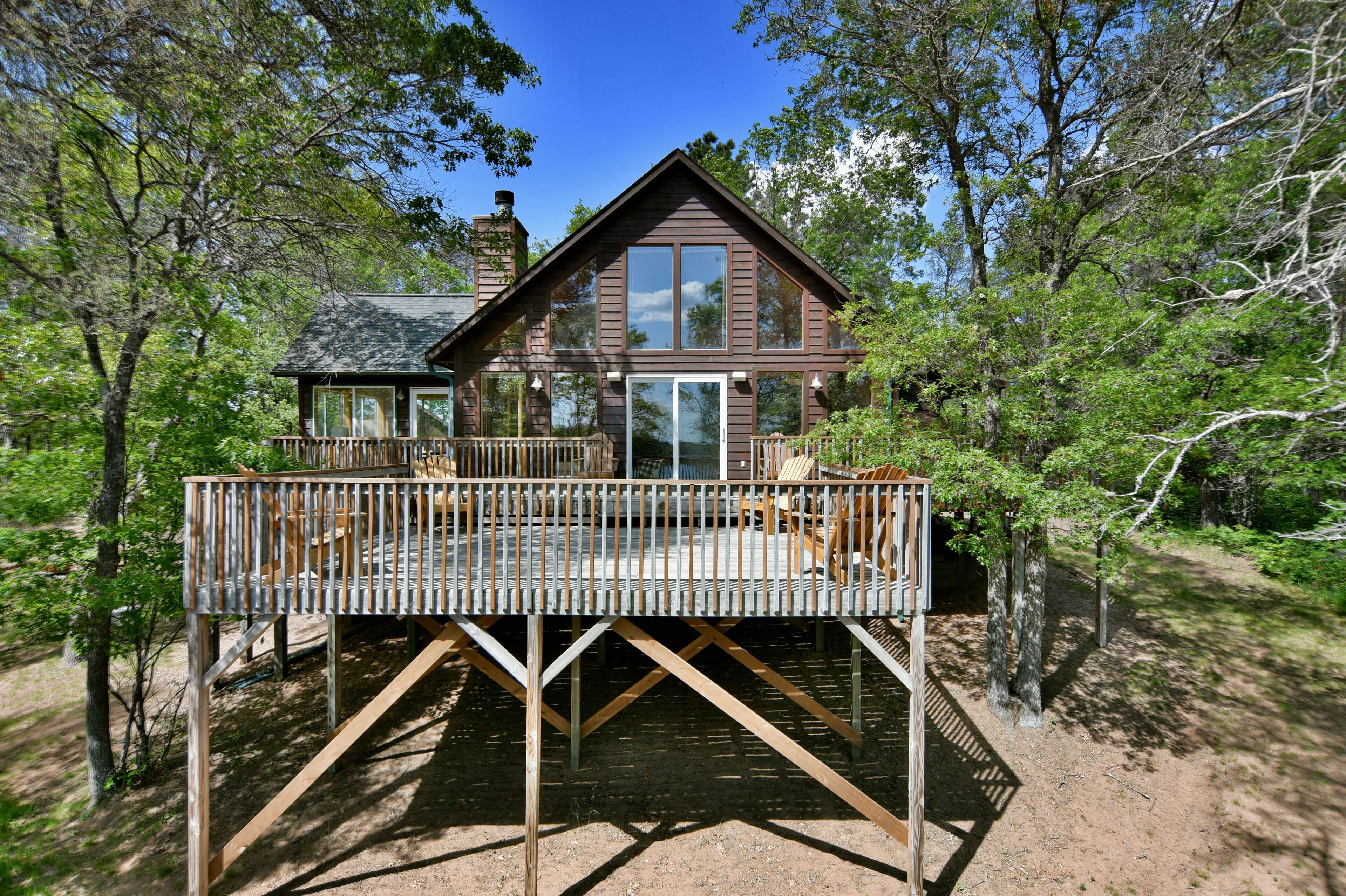 A wooden cabin with a deck, surrounded by trees.