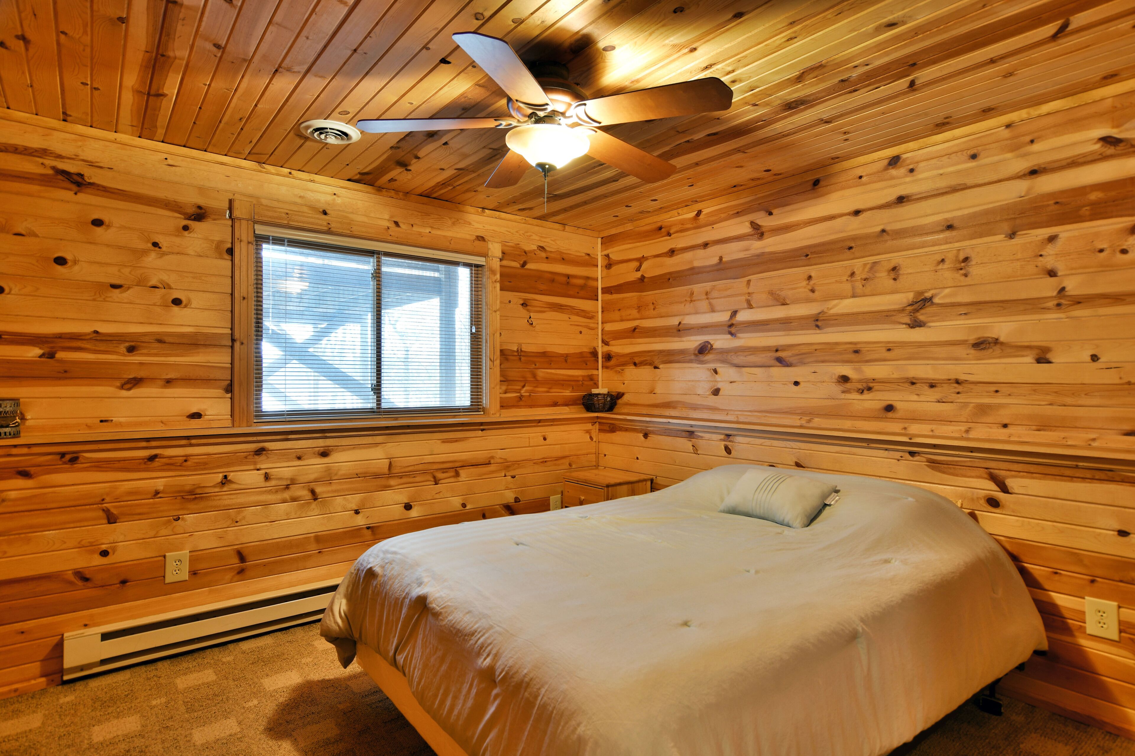 A wooden-paneled room with a bed, a ceiling fan, and a window.