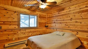 A wooden-paneled room with a bed, a ceiling fan, and a window.