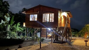 Ein Holzhaus mit einer Treppe, die zu einem Balkon führt, umgeben von tropischen Pflanzen.