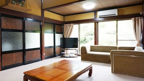 Un salon de style japonais traditionnel, avec un sol recouvert de tatamis, une table basse en bois, un canapé et un téléviseur.