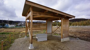 Un pavillon en bois doté d’un toit incliné, d’un banc en béton et d’un sol en gravier.