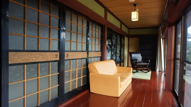 Une pièce de style japonais traditionnel, avec un sol recouvert de tatamis, un canapé, des portes coulissantes à motifs géométriques et une vue par les fenêtres.