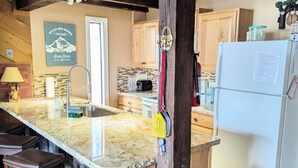 Eine Küche mit Marmorarbeitsplatte, Holzbarhocker, einer Edelstahlspüle und einem weißen Kühlschrank.