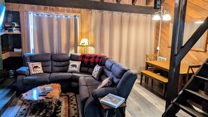 Ein gemütliches Wohnzimmer mit einer Eckcouch, einem Couchtisch und einem Essbereich mit Holztisch und Bänken.