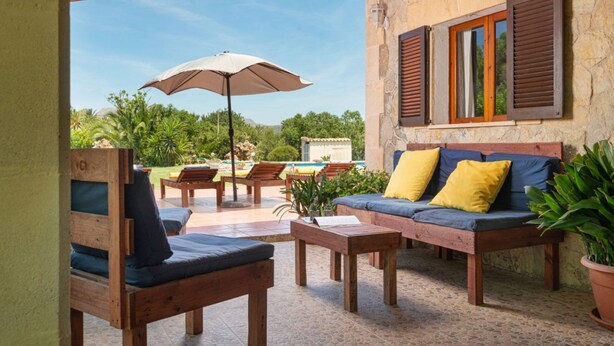 An outdoor patio area with wooden furniture, a stone wall, and a view of a pool. - Rural retreat in the heart of nature: enjoy tranquility and privacy (Pollença)