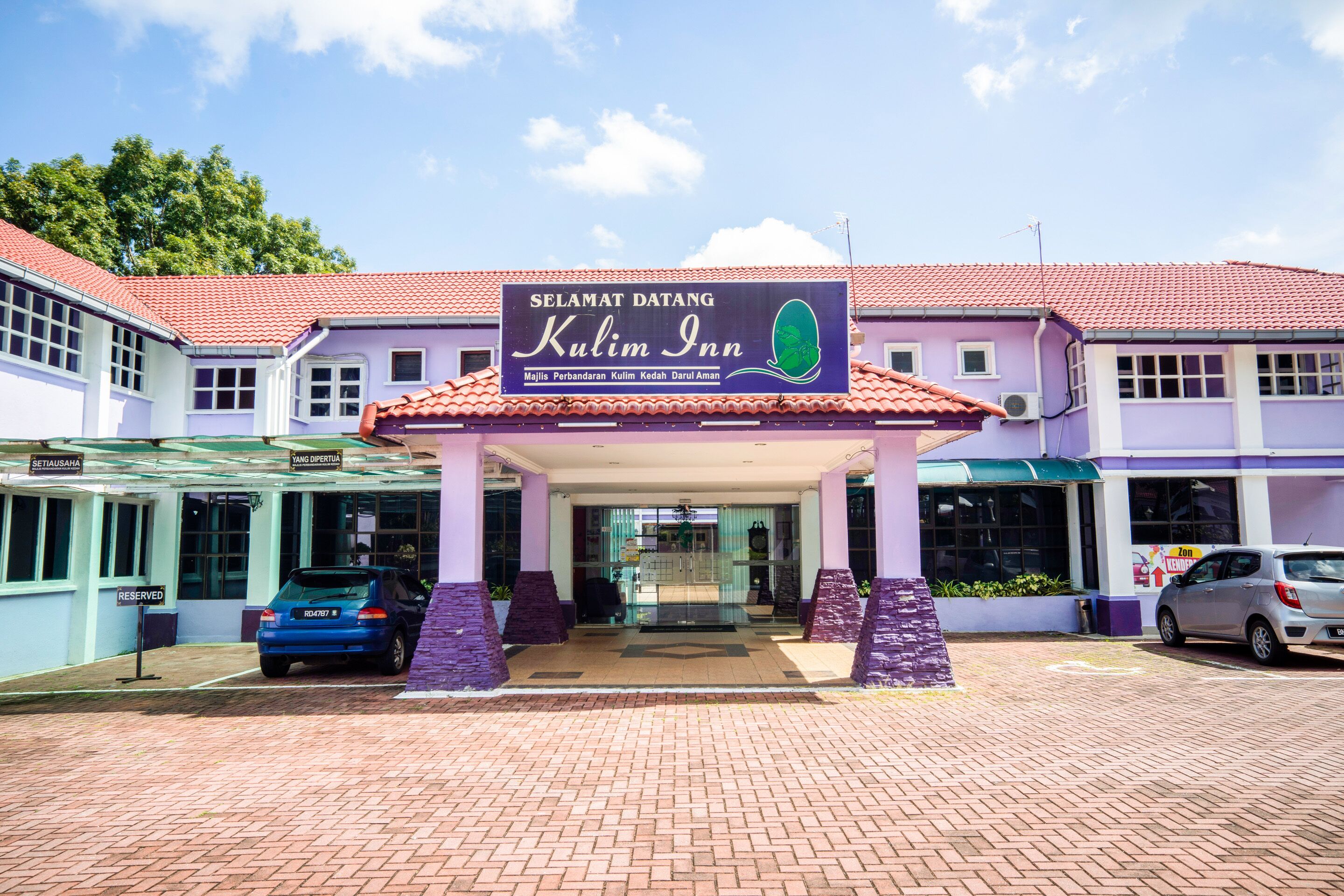 A hotel entrance with a sign reading "Kulim Inn" and a car parked in front.