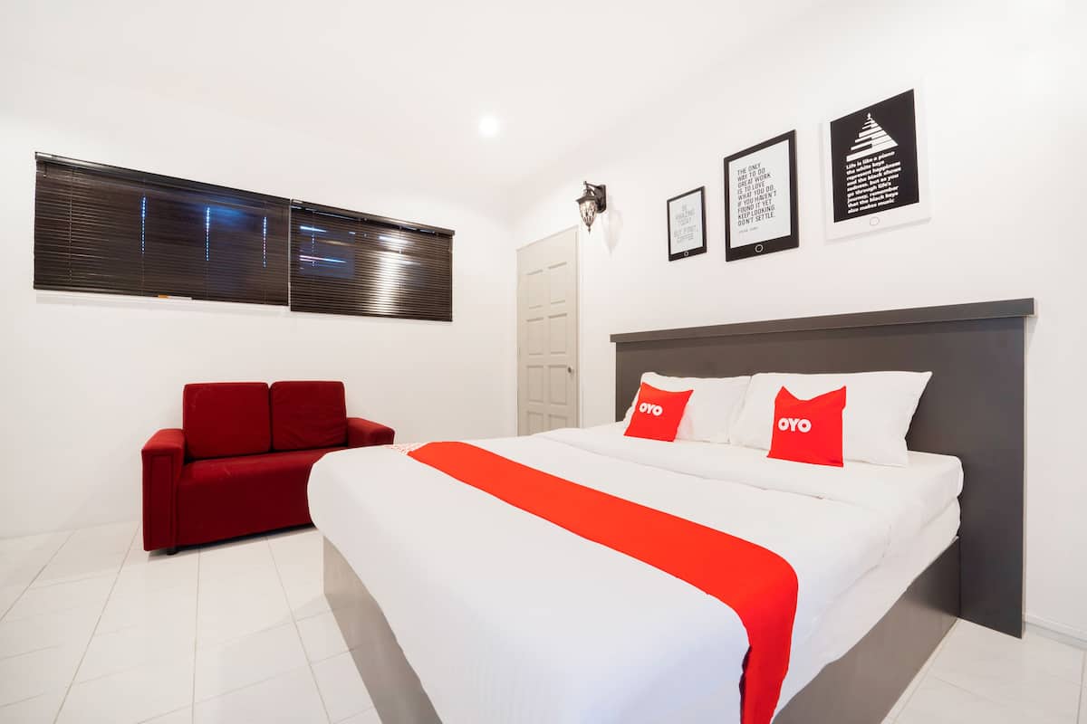 Habitació d'hotel moderna amb un llit gran, un sofà vermell i una finestra amb persianes.